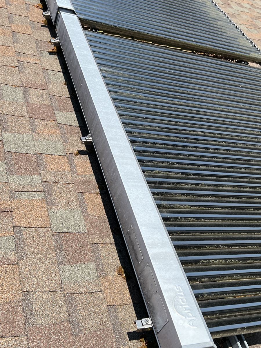 Rows of black evacuated glass tubes on an asphalt shingle roof, with a galvanized manifold box along the edge carrying the Apricus name